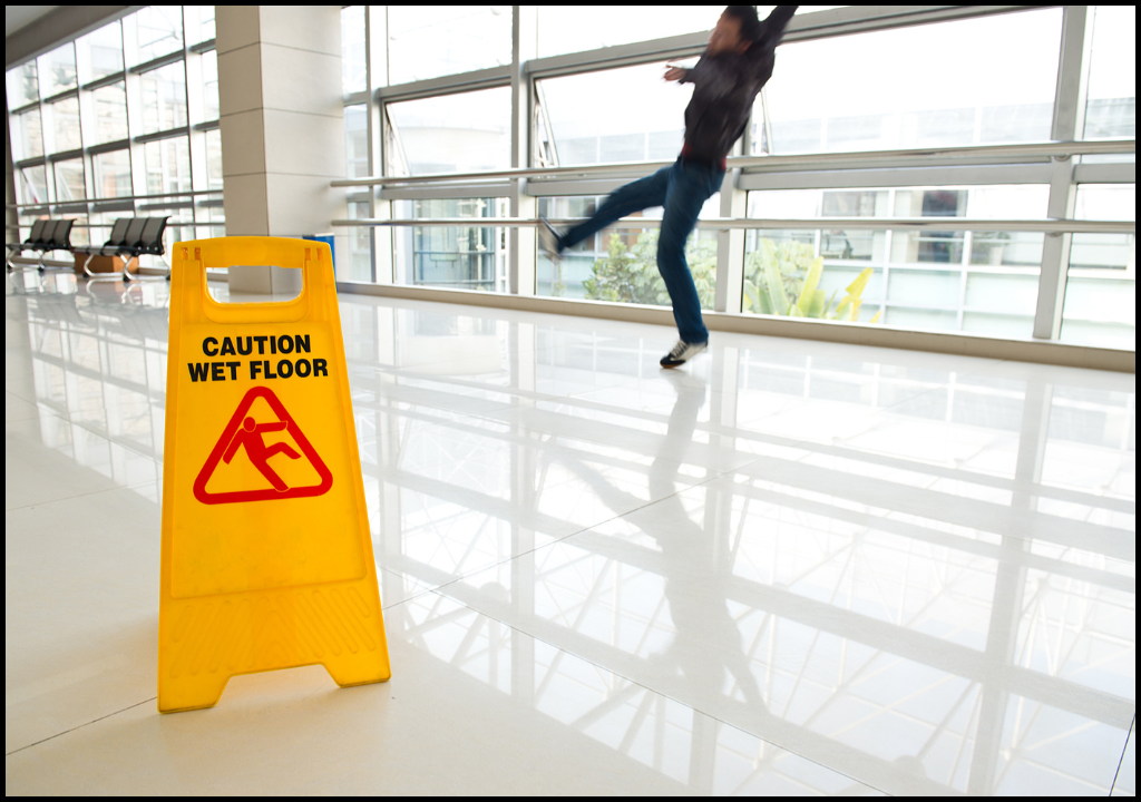 A man experiencing a slip and fall on white tile. A "Caution Wet Floor" sign is in the foreground.