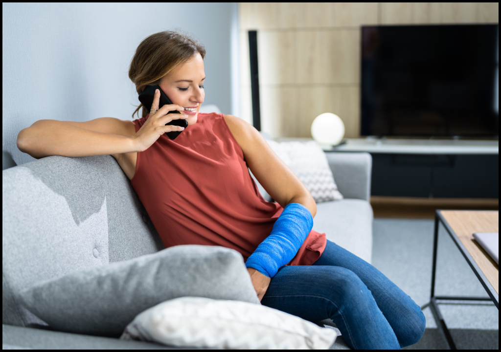 Woman sitting on grey couch with a cast on her arm. She is on the phone.